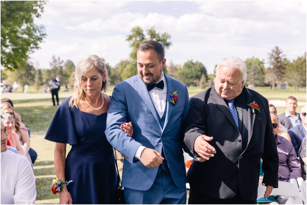 Groom walking down isle with parents at Columbine Country Club
