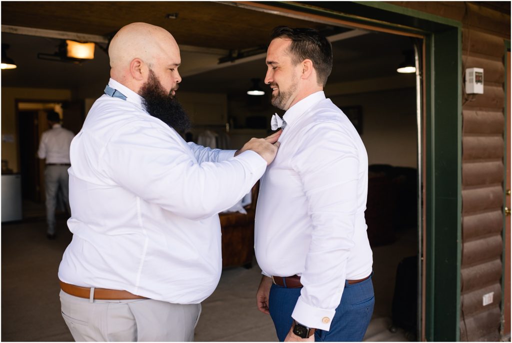 Groom getting dressed for wedding with help from groomsmen.