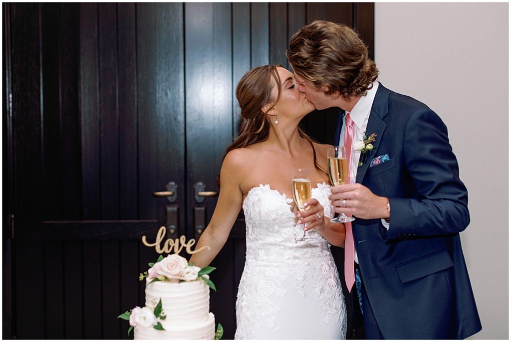 Bride and groom cutting cake designed by Cornerstone Chocolates & Confections and drinking champagne. 