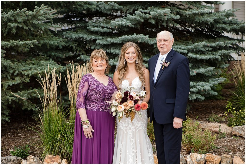 Bride wearing wedding dress from Town and Country Bridal with her mom and dad holding bouquet by Lace and Lilies Flowers.