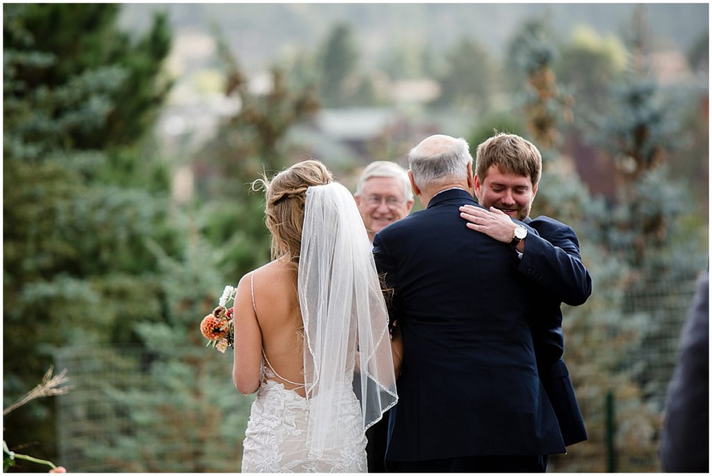 Groom wearing suit from Jos A Bank hugging father at wedding in the Stanley Hotel in Estes Park.