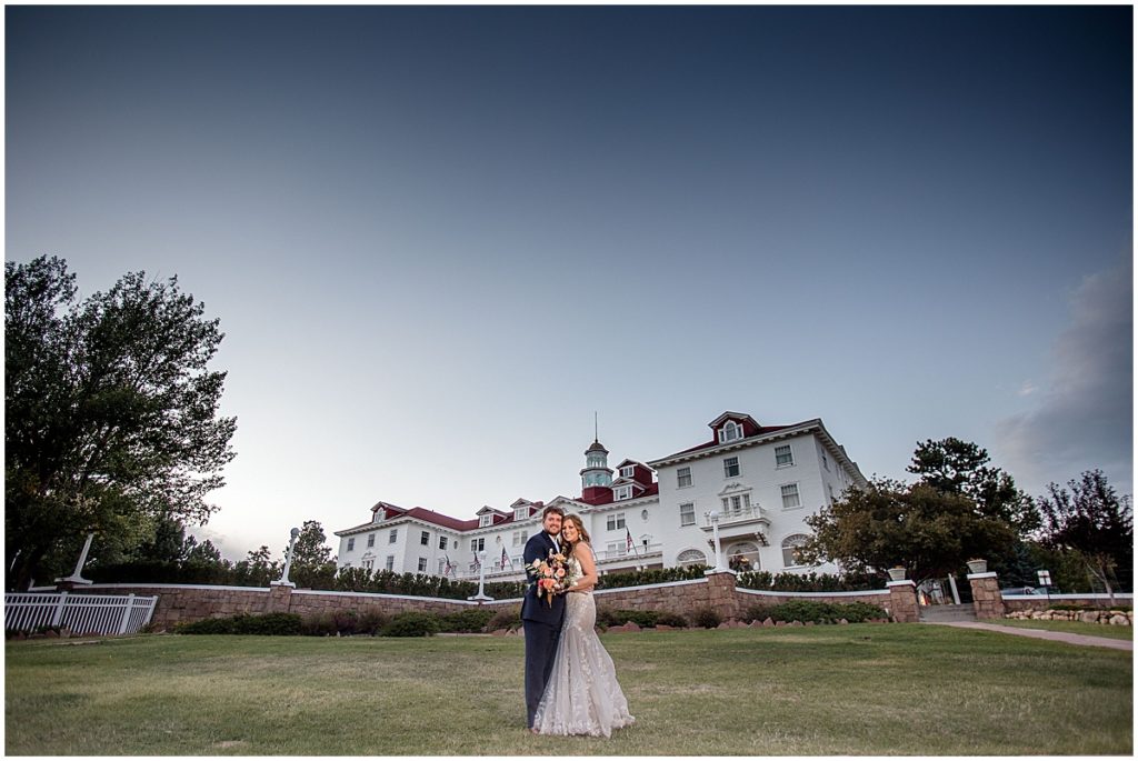 Bride and groom outside at the Stanley Hotel in Estes Park.  Bride is wearing dress from Town and Country Bridal holding bouquet from Lace and Lilies Flowers.  Groom wearing suit from Jos A Bank.