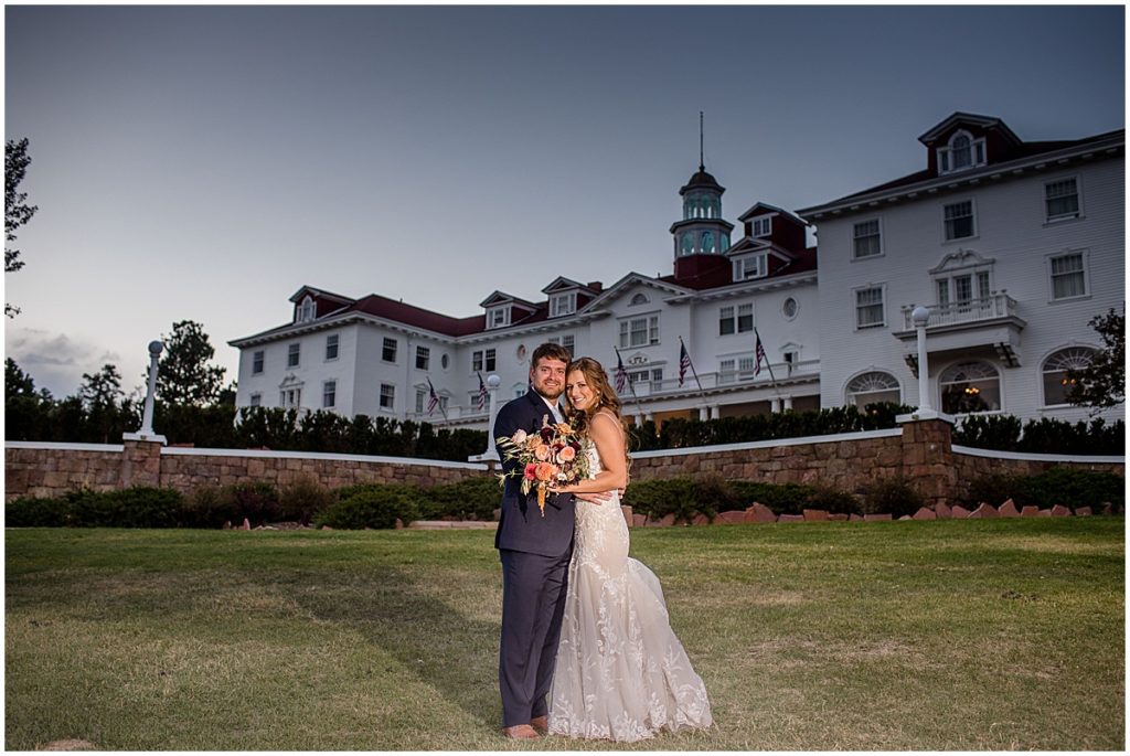 Bride and groom outside at the Stanley Hotel in Estes Park.  Bride is wearing dress from Town and Country Bridal holding bouquet from Lace and Lilies Flowers.  Groom wearing suit from Jos A Bank.