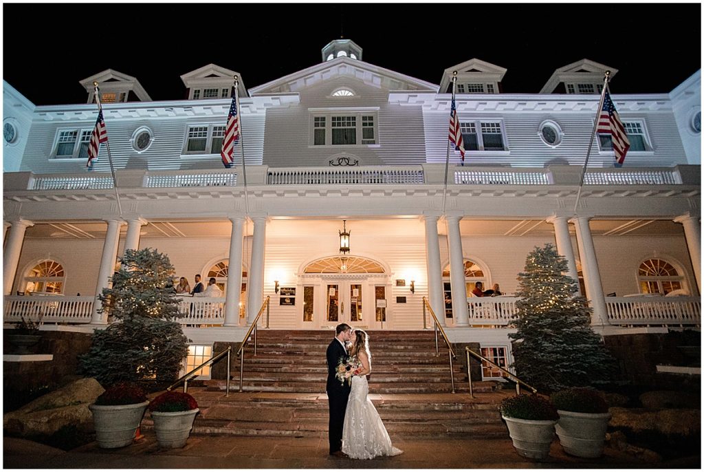 Bride and groom in front of the entrance at the Stanley Hotel in Estes Park.  Bride is wearing dress from Town and Country Bridal holding bouquet from Lace and Lilies Flowers.  Groom wearing suit from Jos A Bank.