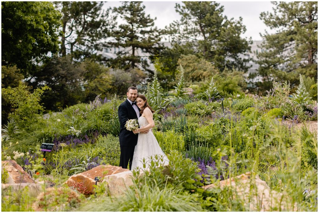 Groom and Bride at Denver Botanic Gardens wearing dress from Little White Dress holding bouquet designed by Plum Sage Flowers.