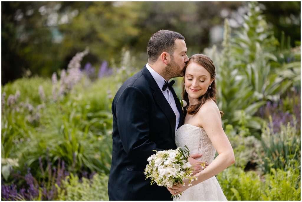 Groom and Bride at Denver Botanic Gardens wearing dress from Little White Dress holding bouquet designed by Plum Sage Flowers.