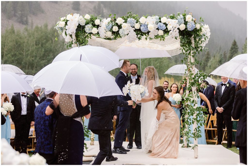 Bride and groom under arch and umbrellas with rain during wedding ceremony