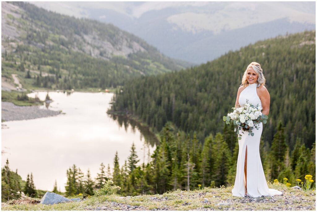 Bride wearing BHLDN dress standing on hill overlooking Blue Lake holding Garden of Eden Floral bouquet