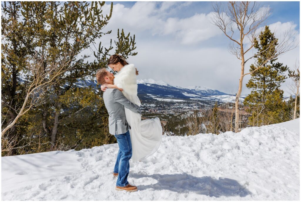 Groom grabbing bride on snow on top of mountain