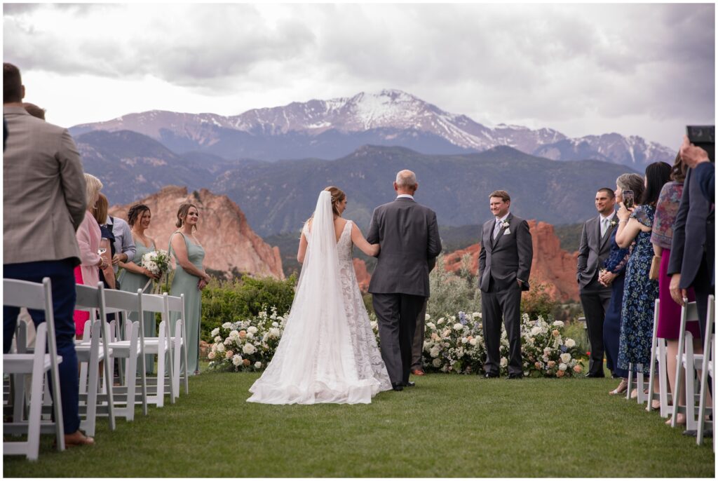 Groom watching bride walking down isle with dad at Garden of the Gods Resort