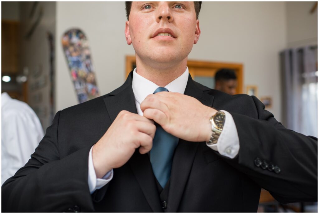Groom putting on suit from Jos A Bank and adjusting tie