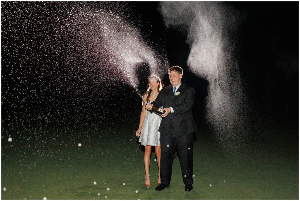 Bride and groom opening bottle of champagne outside at night in Keystone Ranch
