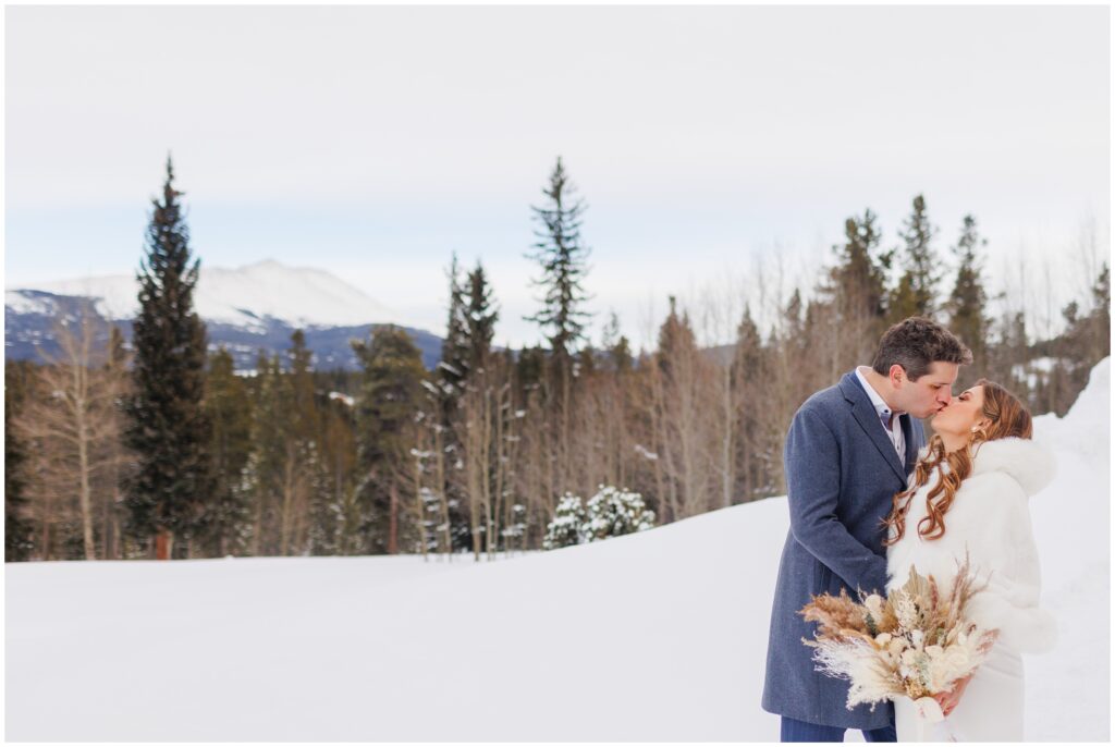 bride and groom kiss on snowy mountain