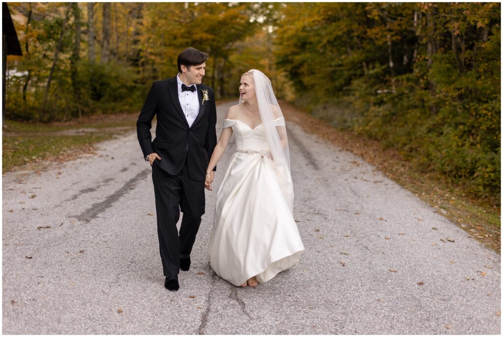 Bride and groom holding hands walking down road surrounded by trees