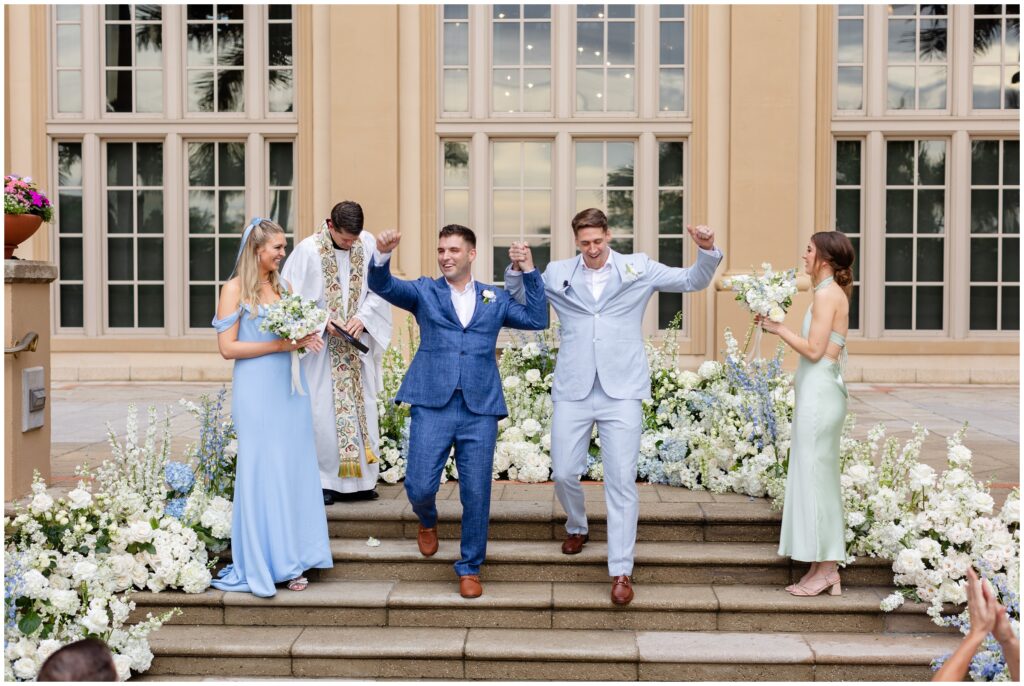 Grooms raising arms in air at the end of wedding ceremony