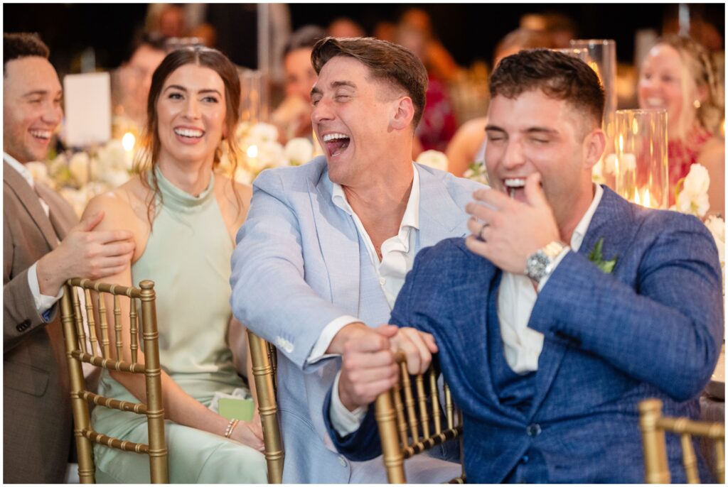 Grooms laughing during speeches at wedding reception 