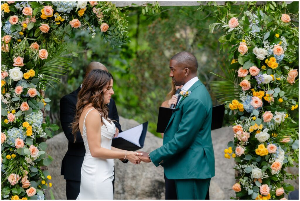 Bride and groom holding hands under floral arch decorated by Belle Terre Floral