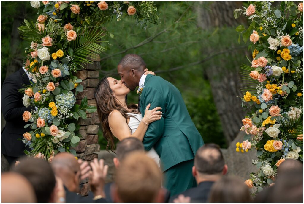 Bride and groom kiss at end of ceremony under floral arch at Boulder Creek by Wedgewood