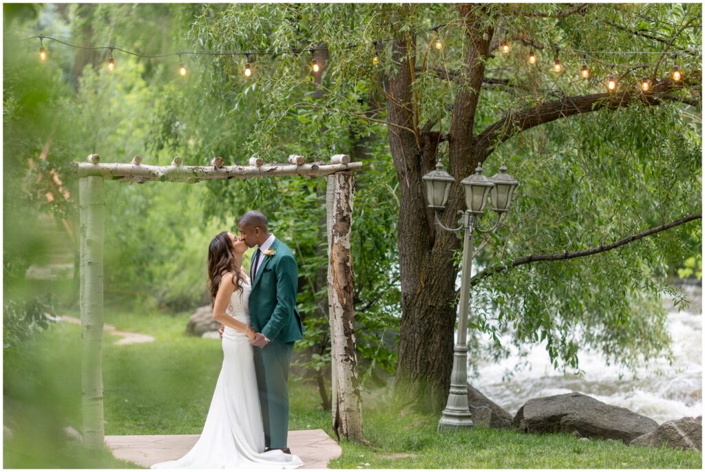 Bride and groom kiss under tree next to river at Boulder Creek by Wedgewood