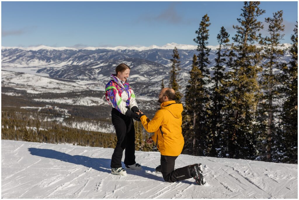 Couple at top of Breckenridge mountain proposal in snow with man down on one knee