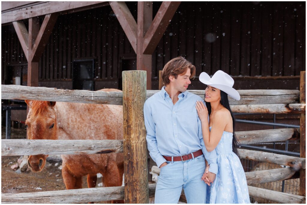 Couple in front of fenced area with horses for engagement session at Devil's Thumb Ranch