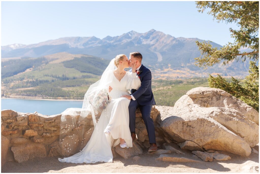 Bride and groom sitting on rock formation kissing