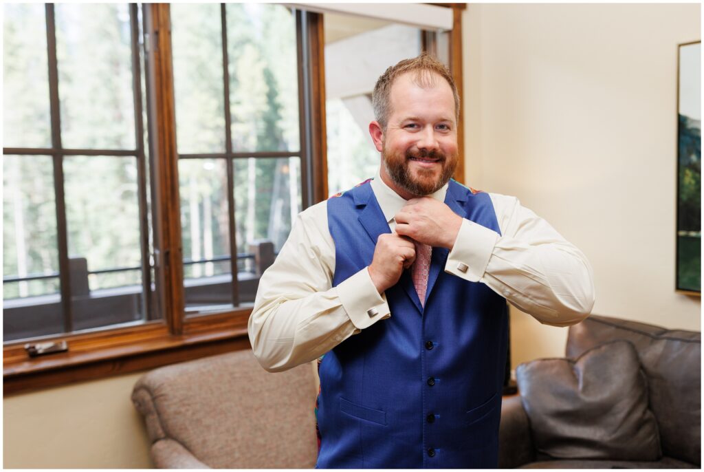 Groom putting on vest and tightening tie for wedding