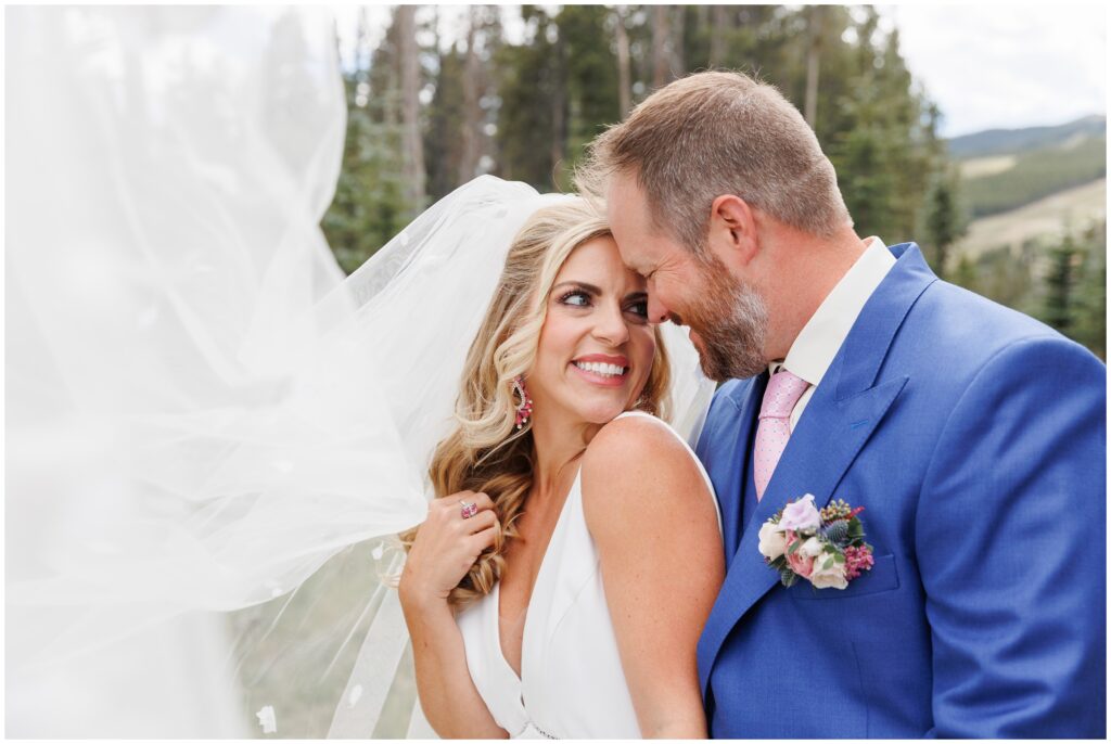 Bride and groom smiling with bride's veil blowing in the air