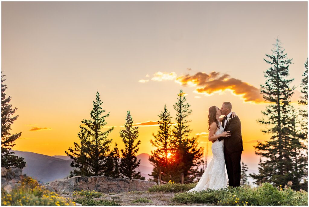 bride and groom standing on mountain top during sunset