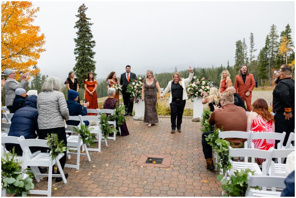 Brides holding hands walking down isle after ceremony